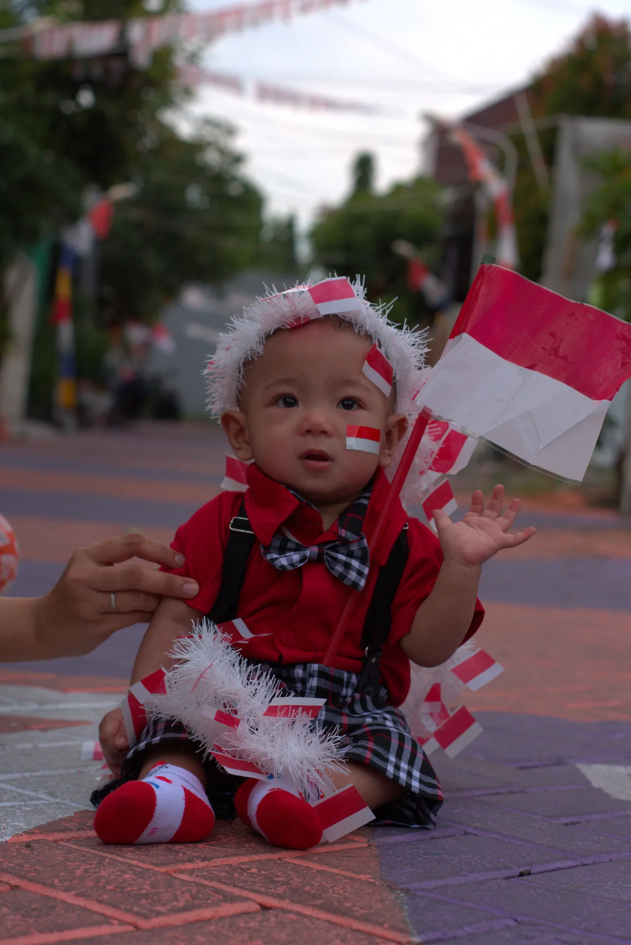 Azel seated outdoors in a red outfit while holding a small Indonesian flag